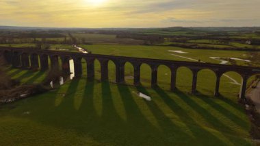 Akşam ışıklarıyla sırılsıklam olmuş manzaralı vadi üzerindeki tren köprüsü. Gün batımında güzel doğa tarafından çerçevelenmiş tren köprüsünün hava manzarası. Tarihi işaretler, ünlü bölge, ulaşım yapısı