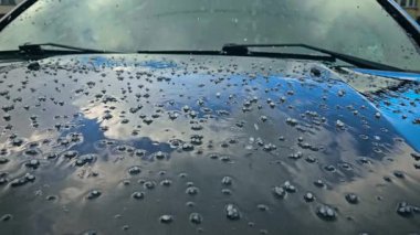 Bahar yağmuru sırasında araba kaputuna çarpmış. Buz topakları ve su damlacıkları araç yüzeyine sıçrıyor. Fırtınalı hava, otomobil boyasına dağılmış dolu taşlarıyla ıslak katman oluşturuyor.