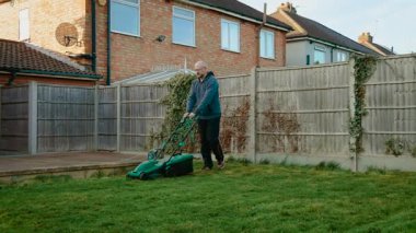 Arka bahçede çim biçen adam elektrikli çim biçme makinesiyle ahşap çitin yanında. Banliyö bölgesinde çim biçme makinesi kullanan bir erkek. Eleman elektrikli çim biçme makinesiyle bahçe çimlerini kesiyor.