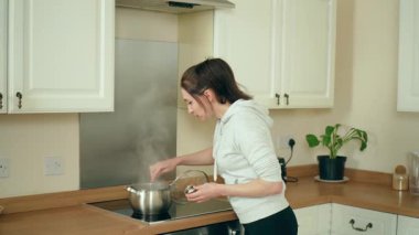 Modern beyaz mutfakta sosis pişiren bir kadın. Çağdaş pişirme alanında kadın sıcak yemek. Hanımefendinin pişirdiği yemekler şık bir mutfak alanında pişiyor.