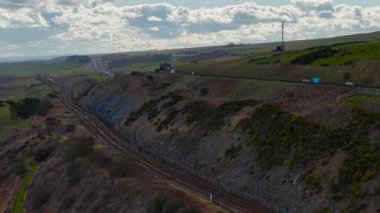 Yolcu treni uçurum boyunca giden araçlarla yol ve mesafe kat ediyor. Uzak tepeler boyunca uzanan demiryolu ve yüksek arazinin yanında giden araçlar. Manzara boyunca seyahat eden tren.