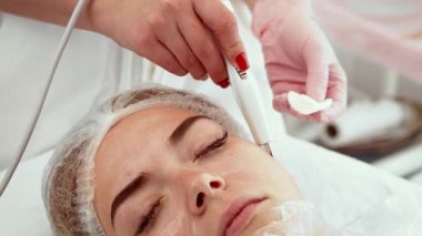 Kaplıca salonundaki yüz bakımı sırasında ultrasonik deri dökücü uygulanıyor. Profesyonel, derin temizlik ve gençleştirme için nazik bir alet kullanıyor. Uzman ileri düzey kullanırken istemci rahatlıyor