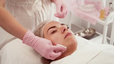 Kadın yüz gerdirme ameliyatı oluyor, profesyonel tedavi sırasında sakince yatıyor. Hasta nazikçe yüz bakımı görüyor, yenilenme sürecinin altını çiziyor. İstilacı olmayan süreçte bireysel rahatlama