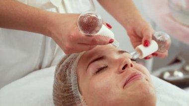 Kozmetik uzmanı, sağlık merkezindeki kadın yüzünde kriyo çubuklar kullanarak cilt serinletme ve gençleştirme üzerinde çalışıyor. Kadın rahat bir şekilde uzanıyor, cilt renginde iyileşme için rahatlatıcı terapinin tadını çıkarıyor. Hasta.