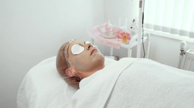 Modern kozmetoloji merkezinde yüz temizleme yapan kadın müşteri. Yenilenme maskesi altında rahatlatıcı pamuk pedlerle rahatlatıcı bir kadın. Derin temizleme ve su kaybına odaklanan tedavi