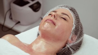 Kadın hasta profesyonel klinik ortamında cilt bakımı sırasında dinleniyor. Bayan müvekkil, rahatlatıcı ve barışçıl bir ifadeyle gençleştirme prosedürü uyguluyor. Bayan güzellik terapisinden hoşlanıyor.