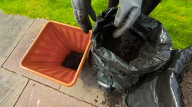 Eller çiçeklere saksı hazırlıyor, kara bahçe çantasından toprak topluyor. Kadın bahçıvanlık sürecine başlıyor, konteynırı besin açısından zengin toprakla dolduruyor. İlkbahar hobisini kucaklayan bir kadın.