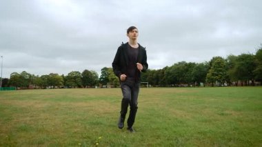 İngiltere 'deki şehir parkında çimenlik alanda koşan bir genç. İngiltere 'deki şehir parkında çimenlikte geriye doğru koşan genç bir adam. İngiltere 'de parkta çimlerin üzerinde geri geri hareket eden bir çocuk. Genç erkek geriye doğru koşuyor.
