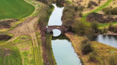 Birleşik Krallık 'taki tarihi kanalın üzerinde kadim tuğla köprü var. Yeşil kırsal kesimde eski duvarcılık yapısını yansıtan durgun su. Kirli yollarla kırsal araziyi kesen dar su yolu.