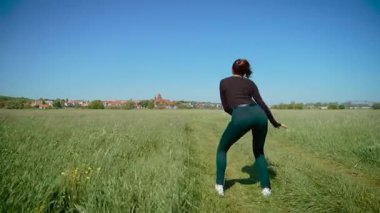 Çimen tarlasında enerjik dans eden bir kadın, coşkuyla kalçalarını sallıyor. Kadın canlı ve canlı hareketler sergiliyor, ritmi ve akışı vurguluyor. Bayan neşe ifade ediyor ve...