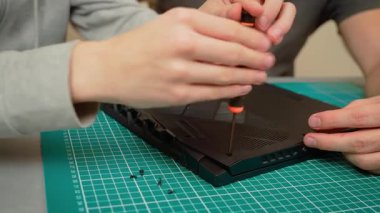 Oğlu, elinde tutarken babasına yardım ediyor. Erkek ebeveyn dizüstü bilgisayarında tornavidayla yardımcı oluyor. Laptop kapağını sökmek için babamla çalışan adam.