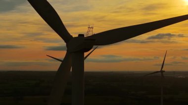 Gün batımında rüzgar türbinleri çiftliğinin manzaralı görüntüsü. Rüzgâr türbini karbon nötr enerjisini dramatik turuncu gece gökyüzü altında iletmek için dönen enerji bıçakları. Dönen rüzgar bıçakları temiz enerji sağlıyor.