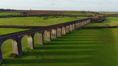 Öğleden sonra güneş ışığı altında verimli kırsal bölgelere uzanan tarihi demiryolu viyaolkü. Günbatımında tarihi Harringworth ve Seaton Köprüsü. Görkemli tuğla köprü sıcak akşam parıltısıyla yeşil tarlaların üzerinde yayılıyor.