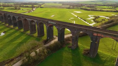 Tarihi demiryolu köprüsü altın günbatımı tonlarıyla birleşiyor. Nefes kesen vadi tarafından çerçevelenmiş demiryolu köprüsünün havadan görünüşü. İkonik konumlar, meşhur bölge, çarpıcı manzaralar arasında ulaşım sistemi