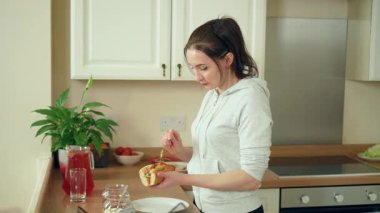 Modern beyaz mutfakta sosisliye sos ekleyen bir kadın. Çağdaş yemek alanında ev yapımı kadın sandviçi. Bayan şık mutfak alanında lezzetli bir şeyler hazırlıyor.