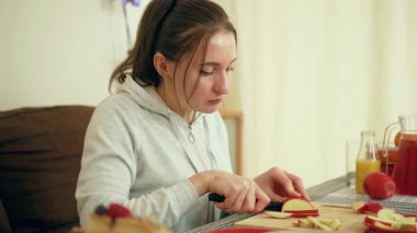 Parlak yemek alanında elma doğrayan bir kadın. Kadın, güneşli ev ortamında tahta tahtada taze meyve dilimleri hazırlıyor. Bayan gevşek mutfak ortamında sağlıklı atıştırmalıklar hazırlıyor.