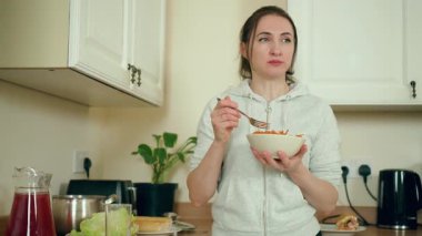Modern beyaz mutfakta havuç salatası yiyen bir kadın. Çağdaş yemek alanında taze sebze yemeğinden hoşlanan bir kadın. Bayan, şık mutfak alanında sağlıklı yemek tadıyor.