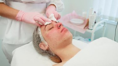 Modern kozmetoloji kadını nazikçe müşterinin alnına pamuk pedi sürüyor. Profesyonel, temiz bir ortamda yüz bakımı yapıyor. Hassas bir teknikle etkili cilt bakımı üzerine uzmanlaşmış.