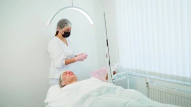 Modern kozmetoloji kliniğinde ıslak peçetelerle yüz temizleme. Kadın cilt bakımını takiben yatakta rahatça uzanıyor. Oturum, optimum sonuçlar için ferahlatıcı ve rahatlatıcı cilde odaklandı