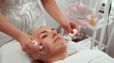 Kozmetik uzmanı, estetik merkezde kadınlara kriyo küreler uyguluyor, ten rengini arttırıyor ve şişkinliği azaltıyor. Kadın rahat bir şekilde uzanıyor, gençleşme için soğutma terapisinin tadını çıkarıyor. İleri derecede yüz tedavisi gören hasta...