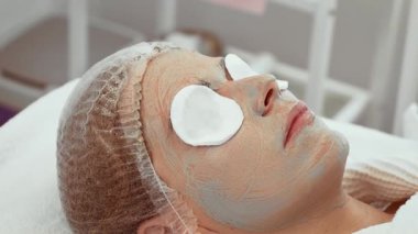Cilt bakımı kliniğindeki ileri yüz tedavisi sırasında kadın pamuk pedlerle rahatlıyor. Kadınlar besleyici maskeyle cilt bakımını yenilemekten hoşlanırlar. Göz alıcı sonuçlar için tasarlanmış profesyonel güzellik hizmetlerinin müşteri yararları