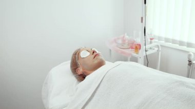 Gelişmiş estetik atölyesinde tedavi gören kadın müşteri. Kadın, iyileştirici pamuk pedlerle rahatlıyor. Susuzluğu arttırıyor. Gençlik parıltısını teşvik etmek için özel dikim prosedürler.