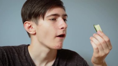 Çocuk yemek sırasında salatalık yiyor. Genç bir erkek, tuhaf bir ifadeyle taze vejetaryen sebzenin tadını çıkarıyor. Rahatlamış yemek anında sağlıklı salatalıkların tadını çıkaran gençler.