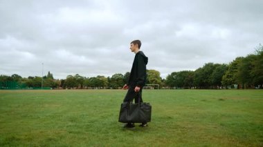 İngiltere 'deki şehir parkında büyük bir çantayla gezen bir genç. İngiltere 'deki şehir parkında çimenlikte büyük bir çanta taşıyan genç adam. Çocuk spor çantasıyla İngiltere 'deki parkta çimlerin üzerinde hareket ediyor. Genç bir erkek, çimenli alanda bavullarıyla geziniyor.