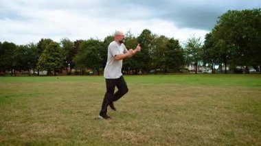 Adam İngiltere 'deki şehir parkında koşuyor ve onaylıyor. Yetişkin bir adam, Britanya 'da yeşil alanda koşuyor ve baş parmağını kaldırıyor. Orta yaş adamı, İngiltere 'nin eğlence bölgesinde koşuyor ve baş parmak işareti yapıyor. Adam koşuyor ve sinyal veriyor.