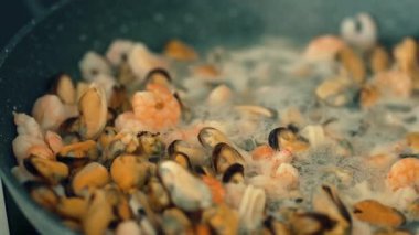 Kabaran sıvının içinde karışık deniz ürünleri kaynıyor. Kızartma tavasında karides, midye ve mürekkep balığı pişirmek. Köpüklü et suyunda kaynatılmış kabuklu deniz ürünleri karışımı. Lezzetli yemekler için taze deniz ürünleri karışımı hazırlıyorum.