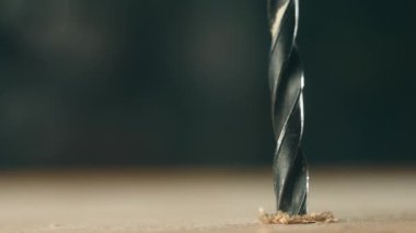 İnşaat sırasında yakın çekim matkabı tahta tahtaya sıkıştı. Makro görüntü sarmal aracı tamir için ahşap yüzeyi kesiyor. Metal parçası donanım sürecinde malzeme aracılığıyla çalışıyor