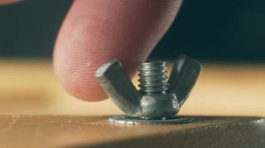 Yakın çekim metal kanat vidaları insan eliyle sökülüyor. Makro görünüm donanım hızlandırıcısı tamirci tarafından alet olmadan elle gevşetiliyor. İnşaat sırasında inşaatçının parmaklarıyla yaptığı çelik cevizi.