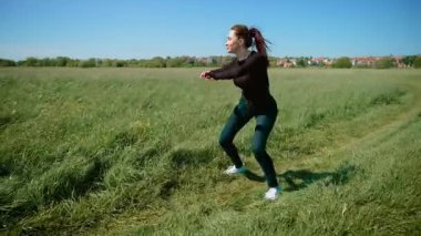 Çimenli alanda son moda dans gösterisi yapan bir kadın, enerjik ve şık hareketler sergiliyor. Sosyal medya izleyicilerini etkilemek için tasarlanmış canlı koreografi uygulayan bir kadın. Kendine güvenen ve yetenekli bir bayan, internette popüler bir dans.