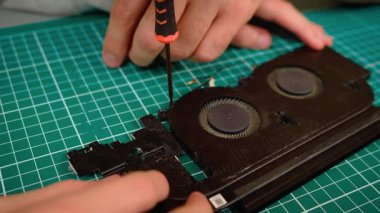 Baba, oğlunun dizüstü bilgisayar soğutma sistemini kurmasına yardım ediyor. Tornavida tutuyor ve vida takıyor. Fan modülünü hizalayan erkek rehber çocuk, kesin montajı sağlıyor. Isıtıcıyı tamir eden çocuk, uygun donanım onarım sürecine odaklanıyor.