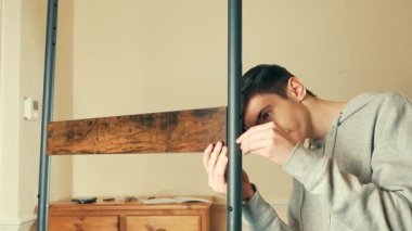 Palto askısındaki tahta tahtayı korumak için tornavida kullanan bir adam. İşlevsel depolama için metal çerçeve oluşturan bir erkek. Adam sağlam ve dayanıklı bir yapı için vida takıyor. Uygun kurulum için hassas hizalama sağlayan işçiler