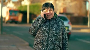 Sokak yakınında akıllı telefondan konuşan bir kadın. Yaşlı bir kadın banliyöye yakın bir yerde telefon görüşmesi yapıyor. Üst düzey bayan sessiz mahalle yolunun yanında dururken cep telefonu kullanıyor.