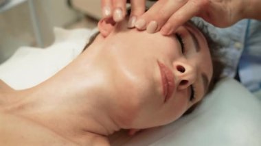 Güzellik kraliçesi müşteriye yüz masajı. Kadın kozmetoloji merkezinde yüz masajından zevk alıyor. Vücut bakımı, cilt bakımı, güzellik tedavisi. Güzellik uzmanı kozmetoloji kliniğinde hasta yüzüne tedavi prosedürleri uyguluyor.