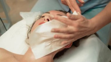 Yüzü hazırlamak için dokuyu kullanan profesyonel biri. Yenilenme için gerekli malzemelerle yüzünü kaplayan bir uzman. Cilt bakımı uzmanı yüzünü hafifçe sarıyor. Terapist yüzüne nazik davranarak durumu optimize ediyor.