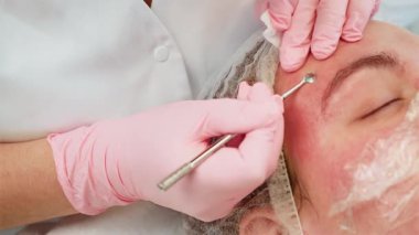 Kadının sorunlu derisinden hassas bir aletle sivilce çıkarmak. Profesyonel, eldivenli elleri dikkatli bir şekilde saf olmayan maddeleri çıkarmak için kullanıyor. Tedavi sırasında cilt berraklığını artırmaya ve lekeleri azaltmaya odaklanan uzman.