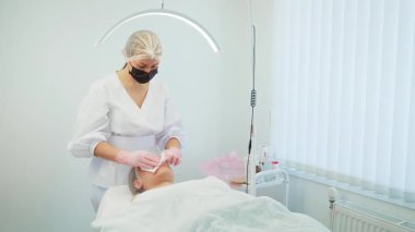 Modern kozmetoloji kliniğinde kırışıklık önleyici ekipman konusunda uzman biri tarafından uygulandı. Uzman cilt bakımı yapılırken, parlak lambanın altında yatan bir kadın. Kırışıklıkları azaltmak ve gençleştirmek için tasarlanmış bir kadın terapisi.