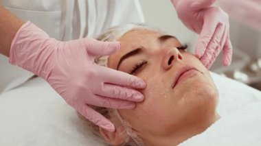 Yaşlanma karşıtı yüz yenileme tedavisi gören bir kadın sakince yalan söylerken uzmanca masaj yaptırıyor. Cilt bakımı uygulanan hasta ince çizgileri azaltmaya ve parıltıyı geri getirmeye odaklanıyor. Profesyonel yüz bakımı sırasında bireysel rahatlama