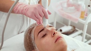 Cilt bakımı kliniğinde güzellik makinesiyle hidrojen maskesi alan hasta kadın. Güzellik uzmanı, gençleştirme tedavisi için gelişmiş teknolojiyi dikkatlice uyguluyor. Yenilikçi hidratlama prosedürleriyle deri sağlığını geliştiren uzmanlar