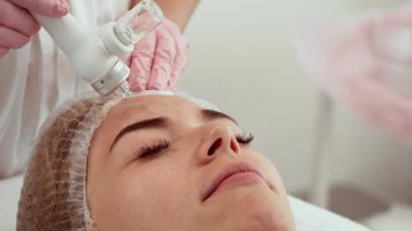 Güzellik uzmanı kadın güzellik kliniğinde hidro cilt bakım aleti kullanıyor. Hasta yüz tedavisi görüyor. İşlem cildin temizlenmesine ve tazelenmesine yardımcı olur.