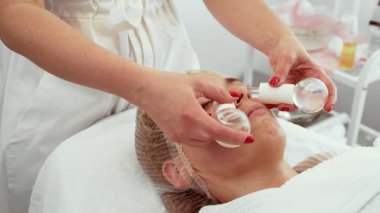 Kozmetik uzmanı yüz yenileme kliniğinde kadın yüzüne buz topu masajı aletleri kullanarak cilt sertliğini ve rahatlığını arttırıyor. Kadın rahat bir şekilde uzanıyor, rahatlamak için serinletici terapinin tadını çıkarıyor. İleri seviye cilt bakımı alan hasta