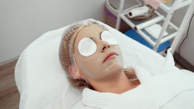 Cilt bakımı kliniğindeki cilt bakımını gençleştirirken uygulanan pamuklu pedlerle dinlenen kadın. Deri hidrasyonu ve onarımına yönelik gelişmiş estetik tedavi gören bir kadın. Müşteri profesyonel ve rahatlatıcı güzellik deneyimlerinden hoşlanır.