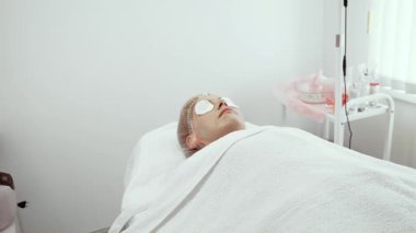 Kadın müşteri bütünsel güzellik merkezinde rahatlatıcı maske altında dinleniyor. Kadın gençleştiriyor ve doğal cilt parlamasını teşvik ediyor. Özelleştirilmiş tedaviler refahı ve uyumu artırıyor