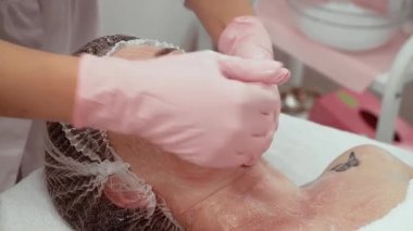 Güzellik uzmanı cilt tedavisi sürecini hassasiyetle ve özenle gerçekleştiriyor. Hasta gençleştirici krem sürerken dinleniyor. Cilt uzmanları parlak sonuçlar için pürüzsüz ve hatta uygulama sağlıyorlar