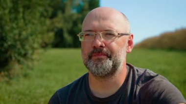 Gözlüklü kel adam yeşil üzüm yiyor, tazeliği ısırıyor. Erkek sulu üzüm tadıyor, doğal tatlılığın tadını çıkarıyor. Açık havada taze yeşil üzümün tadını çıkaran adam, lezzetli tadı takdir ediyor.