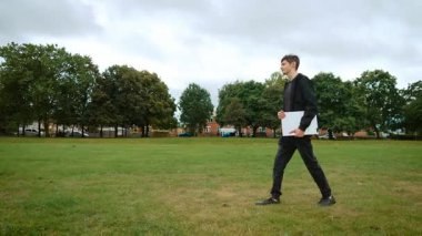 İngiltere 'de parkta not defteriyle yürüyen bir genç. İngiltere 'de çimlerin üzerinde defter taşıyan genç bir adam. Çocuk not defteriyle İngiltere 'de parkta hareket ediyor. İngiliz parkında elinde defterle dolaşan genç bir erkek.