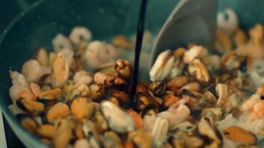 Kaynayan deniz ürünlerine soya sosu döküyorum. Kabaran midye ve karidese koyu baharat ekliyorum. Kabuklu deniz ürünlerinin üzerine tuzlu su serpiyor. Zengin soya ile deniz mahsullerinin lezzetini arttırmak.